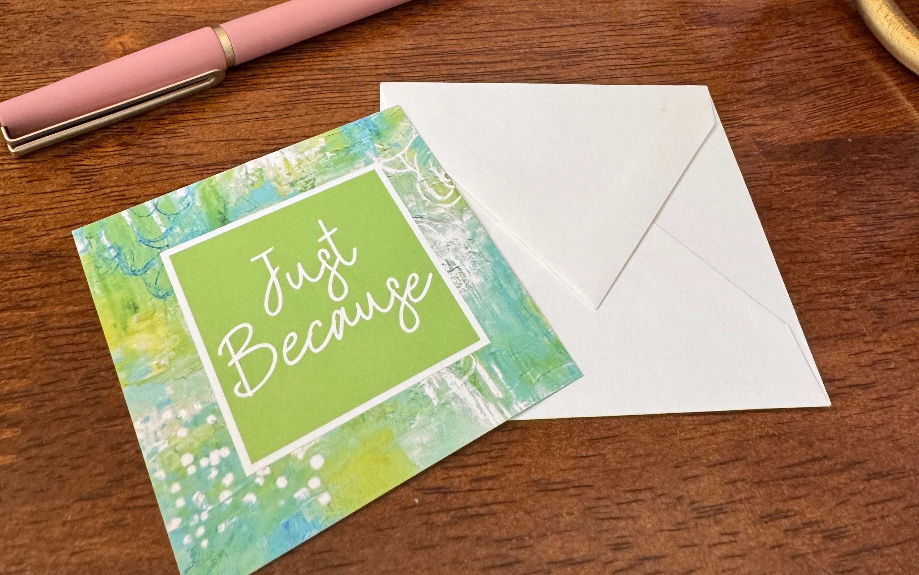 Note card with 'Just Because' text on a wooden surface with a pen and decorative items.